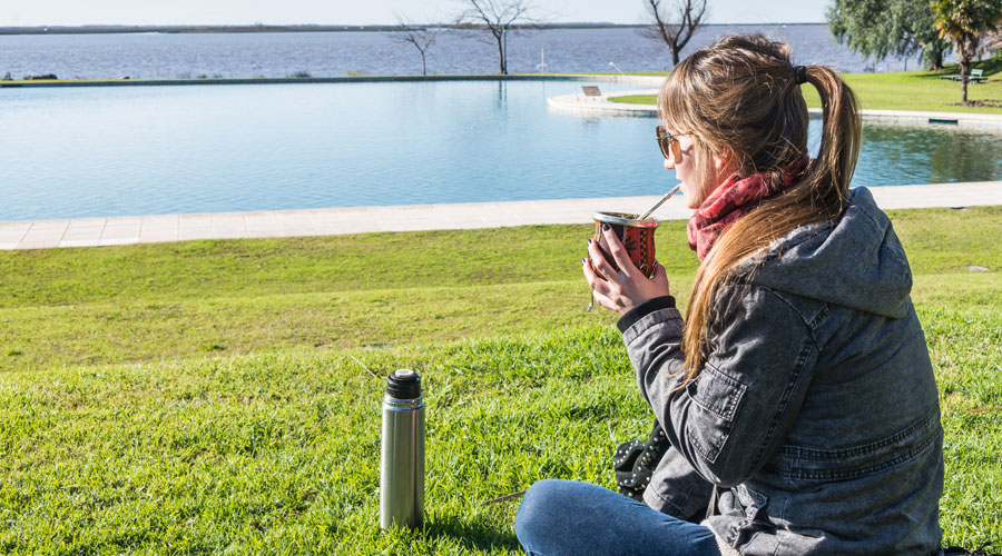 jovem mulher sentada em um parque, tomando chimarrão e apreciando a paisagem