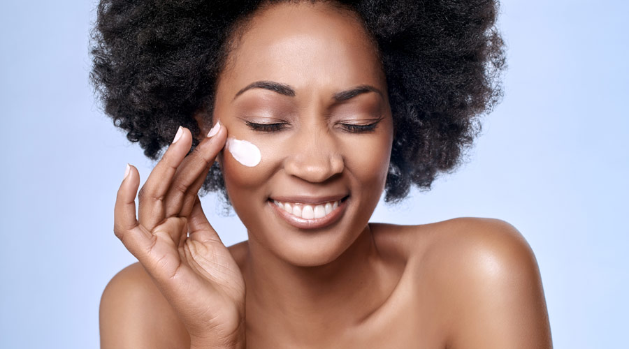 Plano fechado mostra mulher negra aplicando produtos para pele com textura em creme