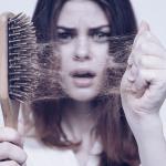 Uma mulher segura uma escova. Em primeiro plano o foco está nos vários cabelos acumulados na escova, enquanto ao fundo a mulher faz uma expressão de desespero.