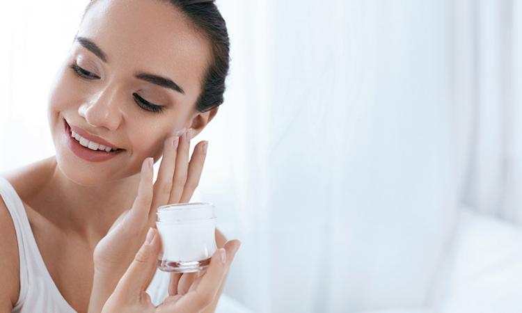 Ácidos para pele: jovem mulher aplica produto no rosto.